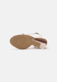 Sandale couleur crème avec un talon bloc transparent, une bride de cheville adjustable et une semelle texturée présentant des motifs en vagues.