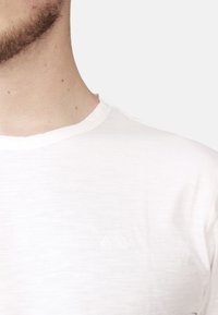 T-shirt bianca in cotone con scollatura rotonda e un sottile logo a rilievo sul petto. Tessuto liscio e leggero.