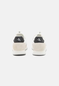 Bílé tenisky s kombinací materiálů, včetně hladké kůže a semiše. Černé akcenty na patě a detail loga na zadní straně.