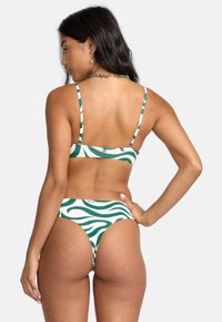 Zelený a krémový bikiny set s vlnovým vzorom, nastaviteľnými tenkými ramienkami a spodnými časťami s miernym zakrytím a nízkym pásom.
