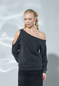 Asymmetrisk svart sweatshirt med avfellende design, myk tekstur og ribbede mansjetter. Slitt hem gir en detaljert finish.
