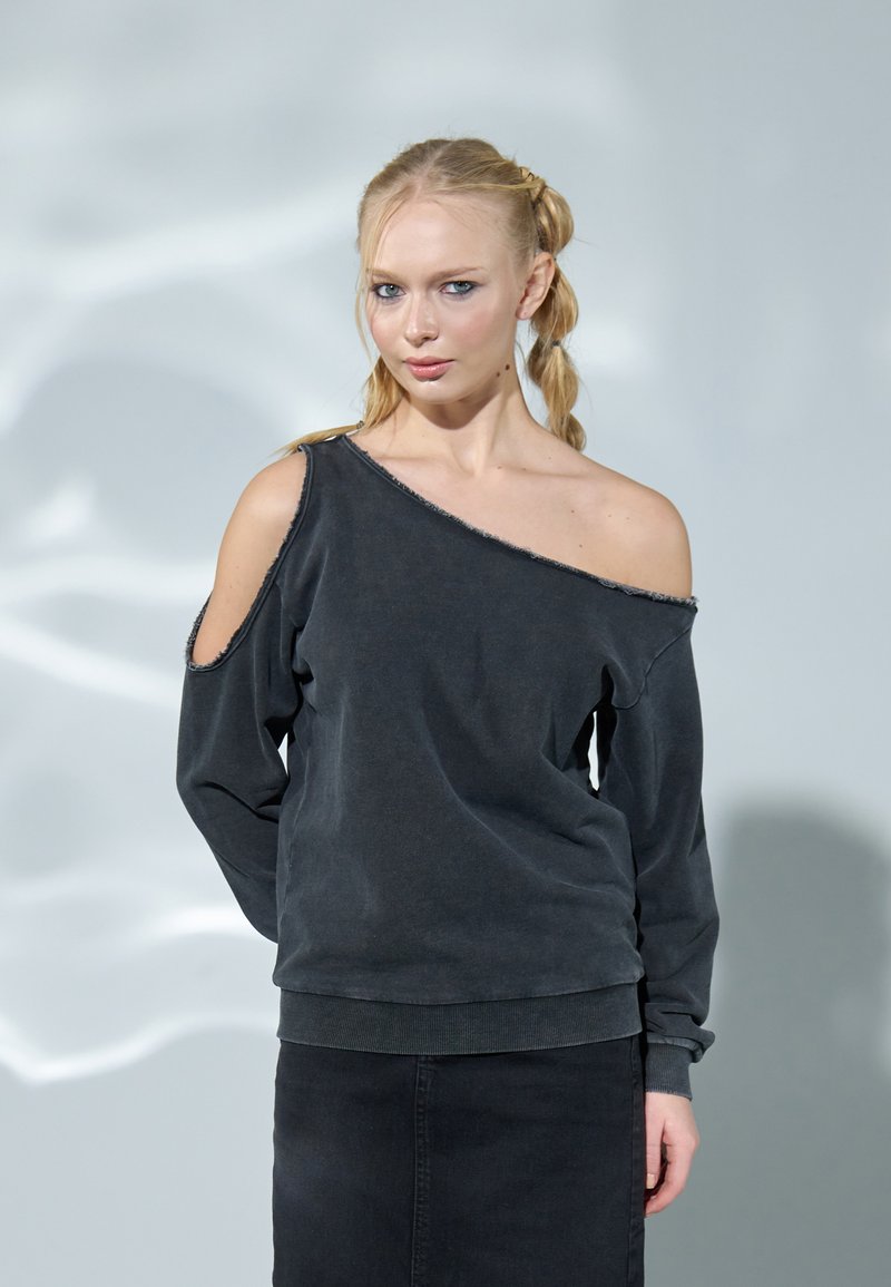 Asymmetrisk svart sweatshirt med avfellende design, myk tekstur og ribbede mansjetter. Slitt hem gir en detaljert finish.