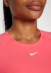 Rosa idrettstopp med rund hals og hvit Nike-logo. Stoffet ser glatt ut med en tettsittende design og kontrastpanel på skuldrene.
