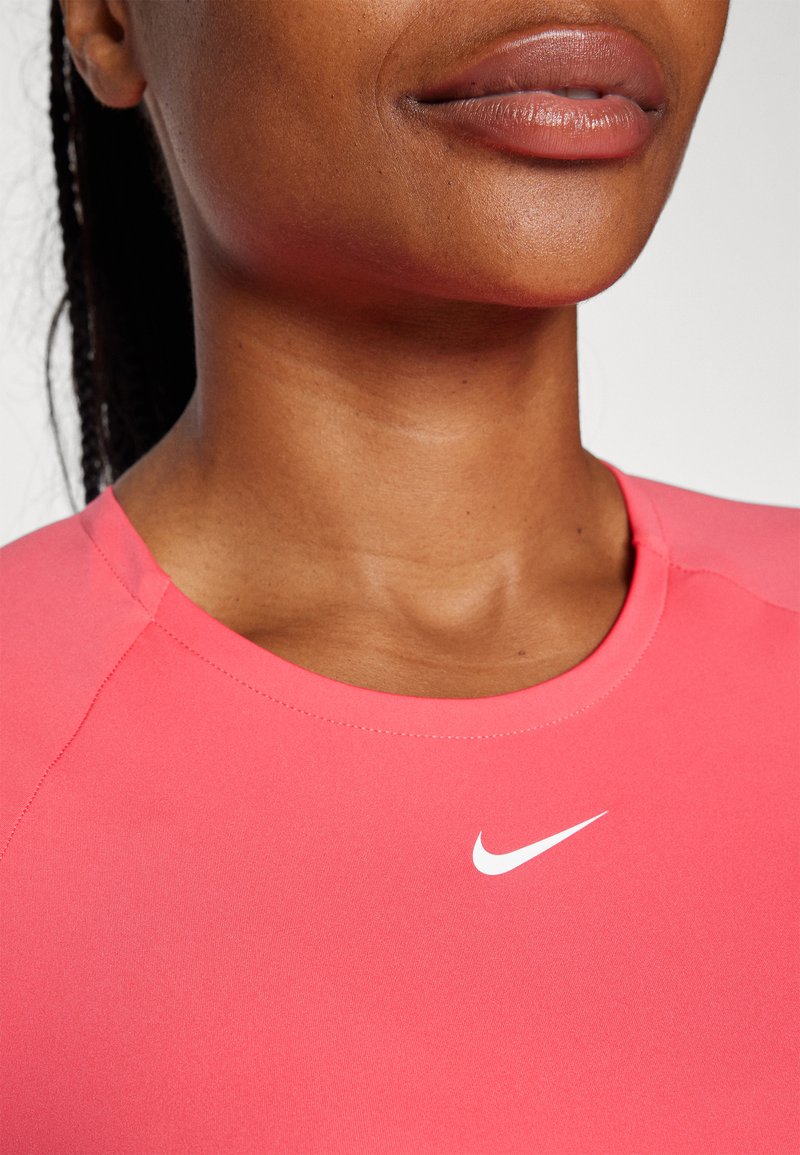 Różowa koszulka sportowa z okrągłym dekoltem i białym logo Nike. Materiał wygląda na gładki, z dopasowanym krojem i kontrastowymi panelami na ramionach.