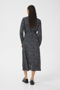 Dunkelblaues Langarmkleid mit Blumenmuster, tailliert mit Gürtel und knielangem Saum. Tragen mit schwarzen Schuhen mit dicken Sohlen.