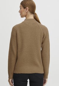 Ribbed knit sweater in light brown, featuring a crew neck, raglan sleeves, and a cropped hem. Made from soft, textured material.