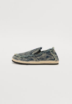 Denim slip-on shoes with a frayed edge, featuring a beige woven jute sole and black rubber bottom. Displayed side view.