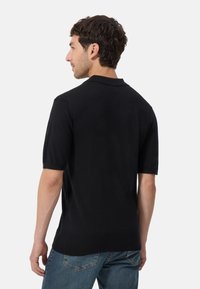 Svart kortärmad polo i ett mjukt trikåtyg med klassisk krage och rak fåll, kombinerad med blå jeans.