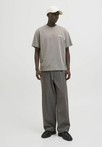 Pelēka pārmērīga T-krekls ar tekstu "UNIVERSAL", apvienots ar brīviem pelēkiem biksēm. Modelis valkā baltu cepuri un melnus apavus.