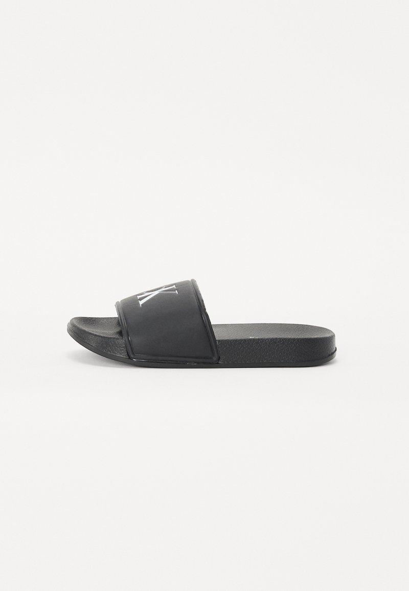 Black slide sandals made of smooth rubber, featuring a wide strap with white logo detailing and a textured footbed for grip.