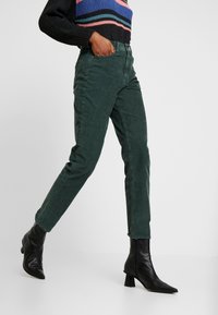 Mörkgrön kordjeans med skräddarsydd passform och rak ben, med hög midja och subtil textur, parat med svarta ankelboots.