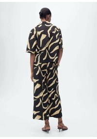 Ensemble deux pièces noir et beige à motif, comprenant un haut à manches courtes et un pantalon large, confectionné dans un tissu texturé avec un design abstrait.