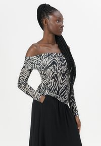 Off-the-shoulder langermet topp i gjennomsiktig svart og hvit zebra mønster. Har en tettsittende bodice og avslappet kant, kombinert med et svart skjørt.