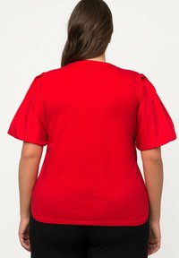 T-shirt rossa con maniche a palloncino corte, scollo rotondo e vestibilità ampia. Realizzata in un tessuto morbido e leggero con una texture liscia.
