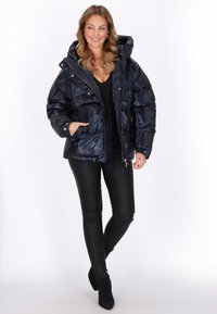 Marineblå puffejakke med hætte, quiltet design, metalliske trykknapper og sidelommer. Parret med sorte tætsiddende bukser og sorte ankelstøvler.