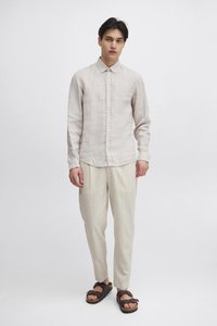 Lysebeige linnedskjorte med knaplukning på kraven, kombineret med matchende løstsiddende beige bukser og brune sandaler.