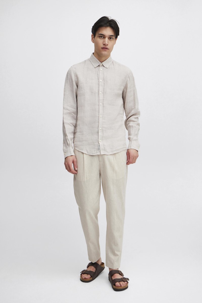 Lys beige lin-skjorte med knapp ned-krage, kombinert med matchende løstsittende beige bukser og brune sandaler.