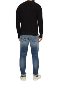 Zwarte textuurtrui, slim-fit blauwe jeans met lichte vervaging, en witte sneakers met een donker accent. Zichtbare stiksels en geribde manchetten.