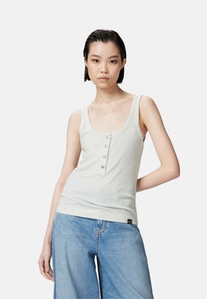 Camiseta sin mangas de color gris claro con escote redondeado y cinco botones en la parte delantera; textura de canalé, diseño ajustado, combinada con jeans de pierna ancha azul.