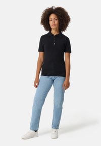 Svart kortärmad polo skjorta med tre knappar i kragen och en figurnära design, kombinerad med ljusblå raka jeans och vita sneakers.