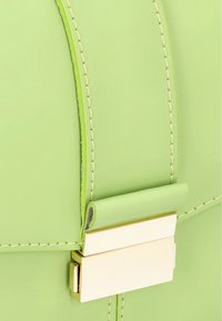 Vihreä nahkainen käsilaukku, jossa on sileä pinta, kontrastoiva keltainen tikkaus ja kultainen metalliklipsi varmistamaan luotettavan sulkemisen.