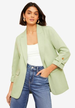 Hellgrüner Blazer mit strukturiertem Design, Ein-Knopf-Verschluss und hochgekrempelten Ärmeln, kombiniert mit hoch taillierten blauen Jeans.