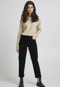 Helles beiges Sweater, schwarze gerade geschnittene Jeans und schwarze Knöchelstiefel. Einfaches Design, glatte Textur, minimale Akzente.