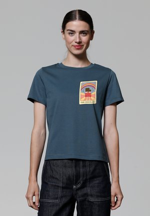 T-shirt en coton teal avec un col rond, des manches courtes, et un imprimé graphique d'une barre de chocolat sur le devant. Équipé d'une coupe décontractée.