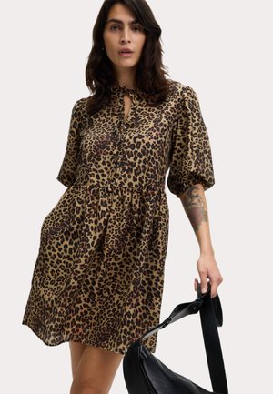 Tijgerprint jurk in tan, met een knoopsluiting bij de hals, korte pofmouwen en een gathered taille. Model houdt een zwarte handbag.