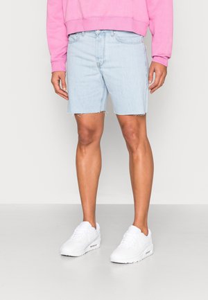 Shorts en denim bleu clair avec ourlet effiloché, design ajusté et poches latérales. Associé à un sweat-shirt rose et des baskets blanches.
