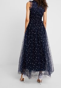 Laivansinis sansihihna iltapuku, jossa on istuva yläosa, kerroksellinen organza-hame ja valkoiset pistekuviot, vyötärö on korostettu ja siinä on läpikuultavia yksityiskohtia.