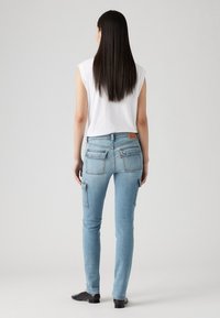 Jeans de mezclilla azul claro con corte ajustado, cinco bolsillos y bolsillos laterales de estilo cargo. Textura suave y diseño clásico.