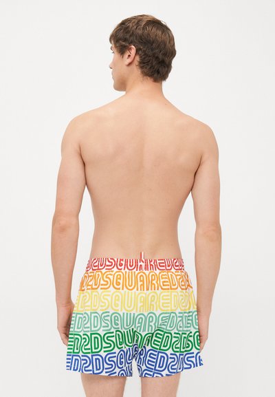 Ung man sedd bakifrån, iförd flerfärgade shorts med upprepande "DSQUARED2"-text i röd, orange, gul, grön och blå.