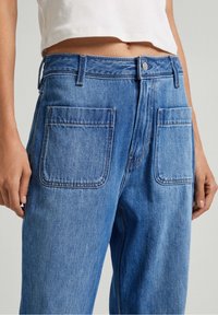Blue denim jeans with a high waist, featuring two large back pockets, classic stitching, and a standard button closure.