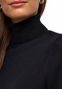 Schwarzer Rollkragenpullover mit gerippter Textur, der eine eng anliegende Passform und eine nahtlose Verarbeitung am Kragen und den Schultern aufweist.