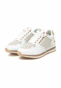 Zapatillas blancas con un diseño floral perforado, acentos dorados y un zip lateral. Presentan una suela beige y una lengüeta de tela texturizada.