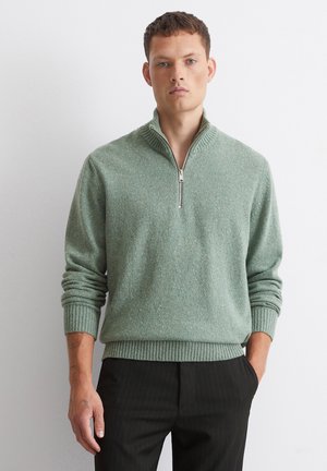 Light green zip-neck sweater with a textured surface, ribbed cuffs, and hem, paired with black pinstriped trousers.