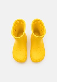 Un par de botas de lluvia de goma amarillas con agujeros de ventilación alrededor de la parte superior y la puntera sobre un fondo blanco.