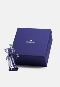 Swarovski crystal figure of a character in purple and green attire, with clear accents. Accompanied by a dark purple packaging box.