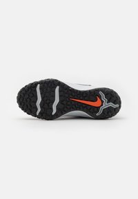 Sapato zole ar melnu teksturētu protektoru, divām pelēkām slīdēšanas vagām un oranžu Nike swoosh logotipu centrā uz balta fona.