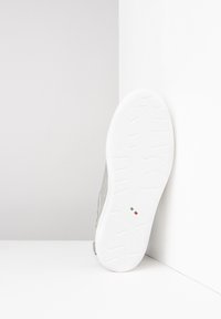 Baskets grises avec un matériau texturé, semelle en caoutchouc blanc présentant un motif en zigzag, et un petit détail du drapeau italien sur la semelle.