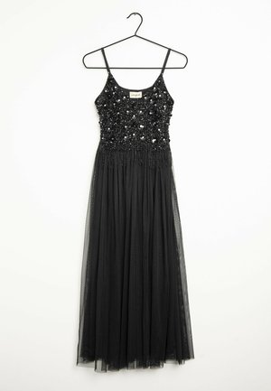 Longue robe de soirée noire à fines bretelles, corsage pailleté et jupe en tulle fluide suspendue sur un cintre noir sur fond blanc.