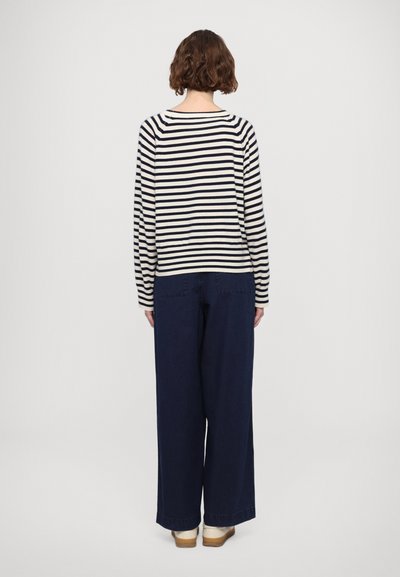 Maglietta a maniche lunghe a righe in navy e crema, abbinata a pantaloni in denim scuri a gamba larga. Vestibilità ampia con scollatura tonda e polsini a coste.