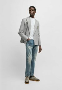 Gray double-breasted blazer over a white shirt, paired with light blue faded jeans and beige sneakers with black accents.