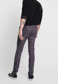 Svart långärmad skjorta i kombination med åtsittande mörka rutiga byxor i nyanser av blått och brunt. Bärs med svarta sneakers, sidosyn.