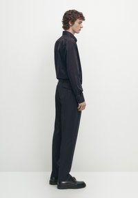 Camicia a maniche lunghe blu navy con righe verticali, abbinata a pantaloni scuri e scarpe nere. Silhouette semplice e dritta con dettagli sartoriali.