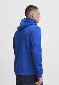 Felpa con cappuccio blu, a maniche lunghe, di colore uniforme e dal taglio leggermente morbido. Presenta una tasca a marsupio e polsini a costine.