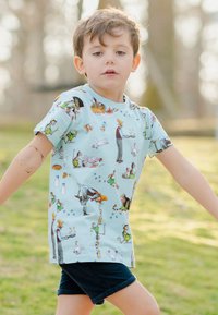 Ljusblå kortärmad t-shirt med olika tecknade bondgårdsscener och karaktärer i en färgglad heltryck; ihop med mörka shorts.