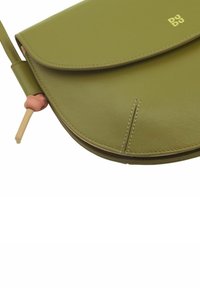 Borsa a tracolla in pelle verde con pattina arrotondata, dettagli di cucitura e un accento rosa pallido sulla tracolla regolabile. Presenta un logo dorato.