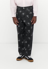 Zwarte denim broek met een volledig bedrukking van biljartballen. Losse pasvorm met vijf zakken, metalen knoop en ritsopening. Gecombineerd met zwarte sneakers.